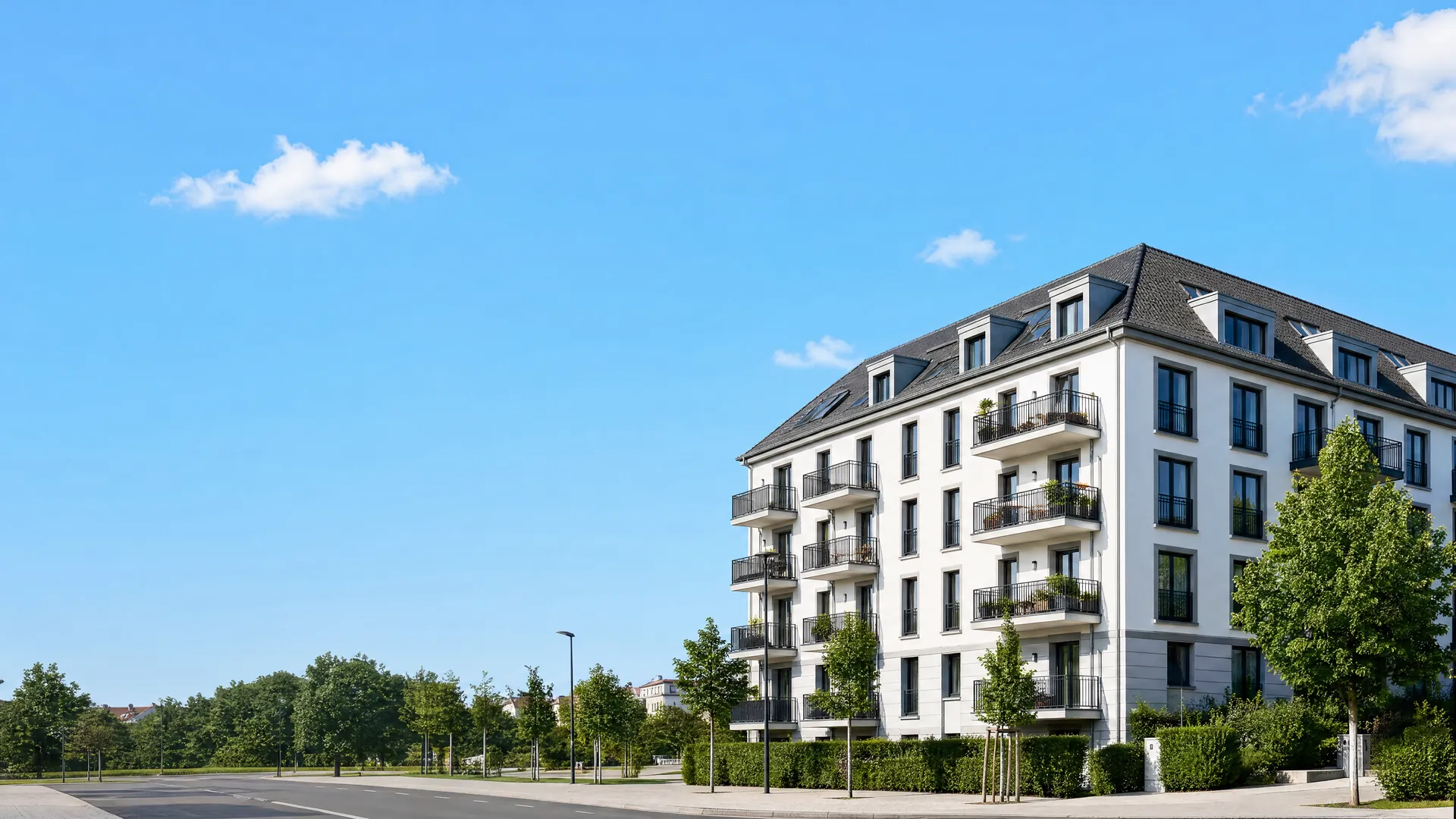 Modernes Wohngebäude mit Balkonen an einer baumgesäumten Straße bei blauem Himmel